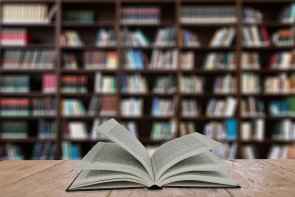 Buch liegt geöffnet auf einem Tisch vor einem Bücherregal