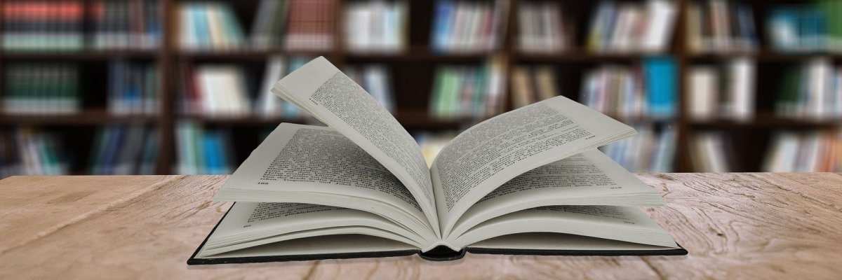 Buch liegt geöffnet auf einem Tisch vor einem Bücherregal