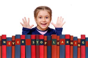 Kind sitzt hinter Büchern die Bücher sind mit dem Schriftzug ,,Never Stop Learning'' versehen